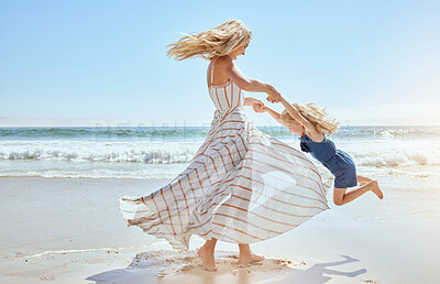 Happy caucasian mother swinging and spinning cute daughter in circles by the arms at the beach. Playful, energetic and joyful kid having fun while bonding with mom on sunny summer vacation outdoors
