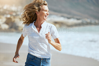 Buy stock photo Cheerful mature woman running on the beach on a sunny day. Beautiful middle aged woman laughing, being active and having fun during summer vacation. Energetic lady spending her free time by the sea