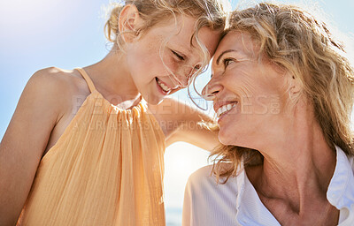 Buy stock photo Cheerful mature woman and little girl talking and sharing a secret while sitting on the beach. Happy little girl smiling while sitting with her mom or grandmother and being loving and affectionate 