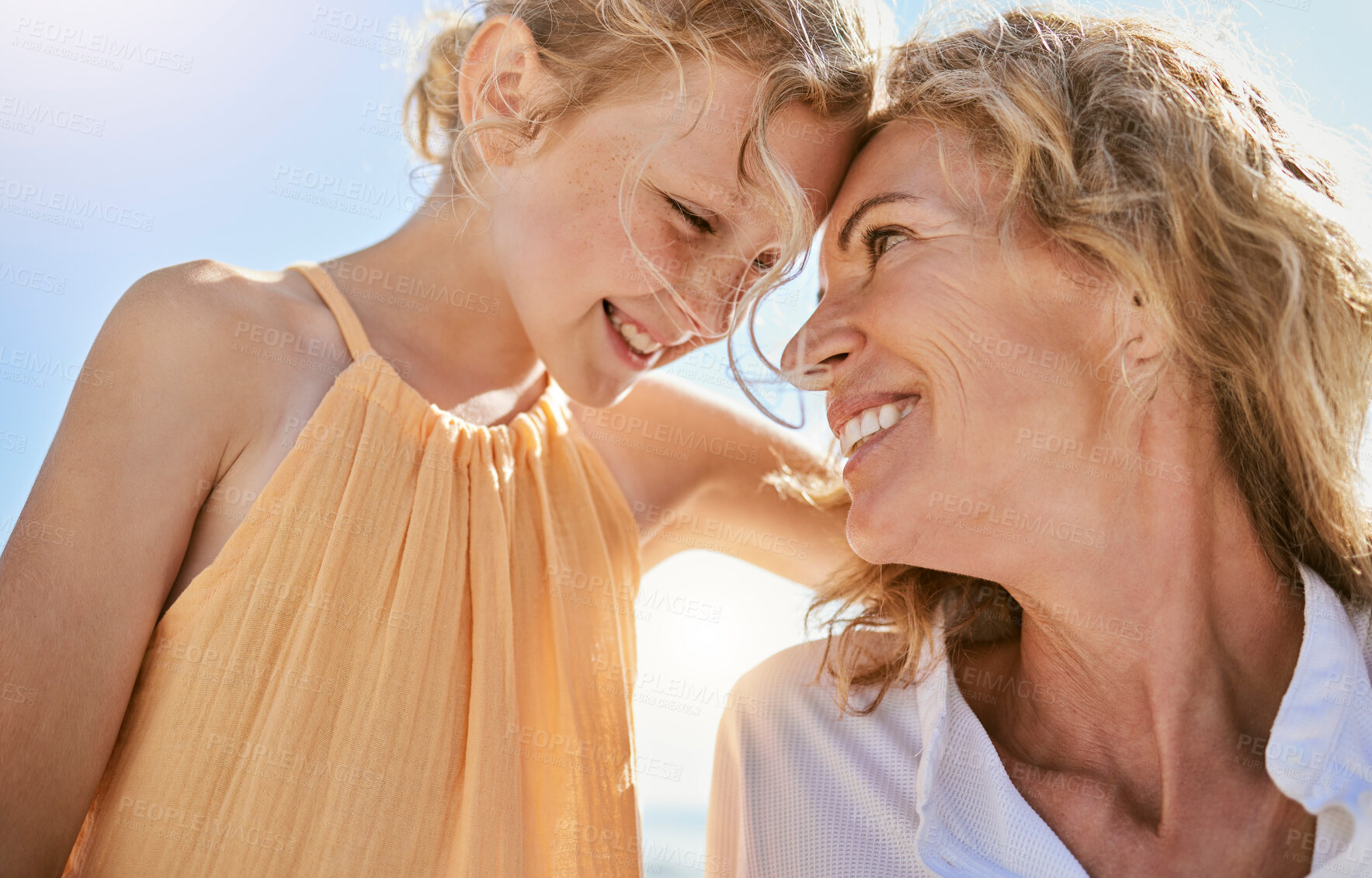 Buy stock photo Cheerful mature woman and little girl talking and sharing a secret while sitting on the beach. Happy little girl smiling while sitting with her mom or grandmother and being loving and affectionate 