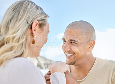 Buy stock photo A young man proposing to his girlfriend at the beach in summer. Happy interracial couple holding hands and smiling. Soon to be husband and wife staring lovingly into one another's eyes outside