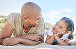 Smiling mixed race single father and little daughter looking at each other while lying on a beach. Adorable, happy child bonding with parent and enjoying vacation. Man and child enjoying free time 