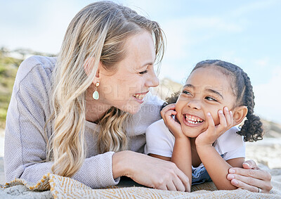 Portrait of a mature mother and her mixed race cute little daughter smiling and lying on the beach. Woman and her adorable girl bonding during a summer day out in the sun. Face to face woman and child