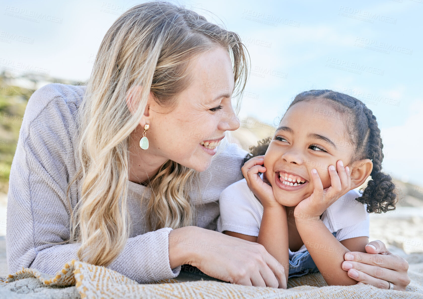 Buy stock photo Mature foster mother and her adopted daughter smiling and lying on the beach together. Woman and her cute little girl bonding during a summer day out in the sun. Face to face single parent and child