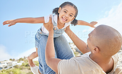 Portrait of adorable little girl from below having fun pretending to fly like a superhero with arms outstretched while being held by her loving dad. Father and daughter bonding together outdoors