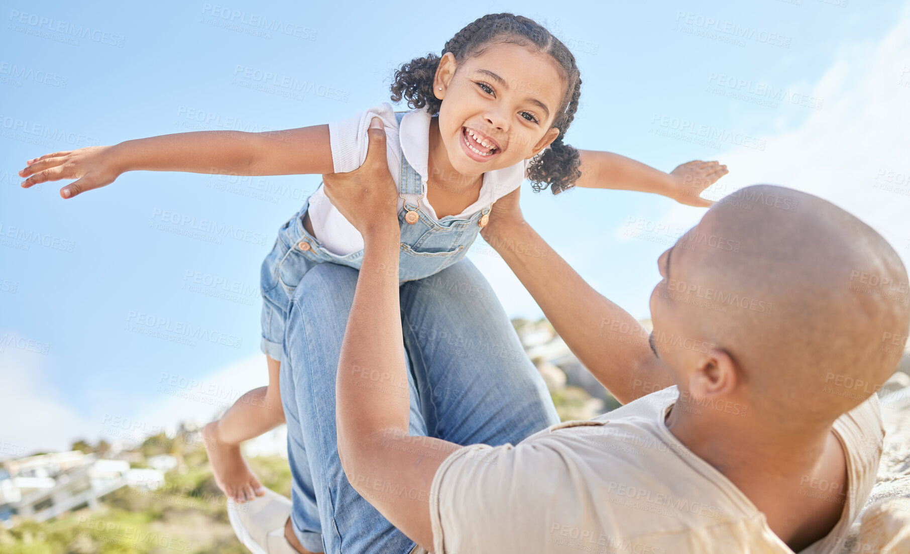 Buy stock photo Father and daughter bonding together outdoors. Portrait of adorable little girl from below having fun pretending to fly like a superhero with arms outstretched while being held by her loving dad. 