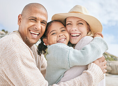 Buy stock photo Portrait of happy interracial family on vacation in summer. Smiling and laughing parents bonding with their daughter outside and having fun on the beach. Cute little girl embracing her mom in a hug