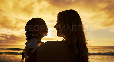 Closeup silhouette of mother and daughter standing on the beach at sunset. Backlit young woman and girl child smiling and talking with the ocean in the background. Single parent and kid on vacation