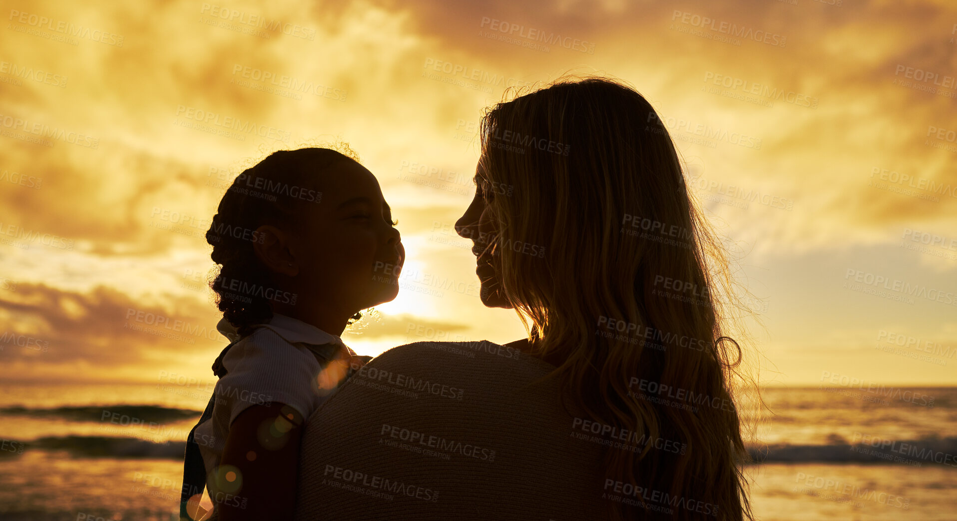 Buy stock photo Closeup silhouette of mother and daughter standing on the beach at sunset. Backlit young woman and girl child smiling and talking with the ocean in the background. Single parent and kid on vacation 