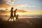 Silhouette of carefree family running and having fun together on the beach. Parents spending time with their daughter while on holiday. Happy little girl playing and bonding with her parents on vacation during a sunset