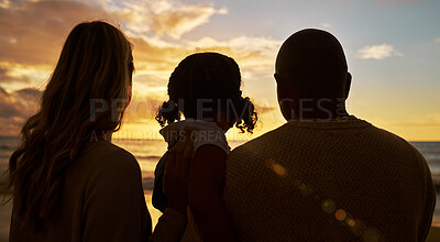 Buy stock photo Silhouette closeup of happy family with one child on the beach looking at view at sunset. Two parents and daughter admiring golden sky and calm sea while enjoying their vacation and spending time