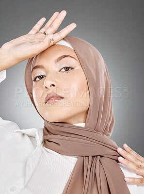 Buy stock photo Modest female model wearing makeup with face covered in traditional hijab. Portrait of one beautiful young muslim woman wearing brown headscarf with hand on forehead against grey studio background.