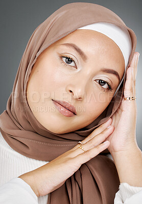 Buy stock photo Portrait of a glowing elegant muslim woman's face isolated against grey studio background. Young woman wearing a hijab or headscarf, showing her eyelash extensions, jewellery and skin routine 