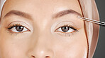 Closeup portrait of unknown muslim woman using tweezers to pluck her eyebrows. Half headshot of confident arab model wearing a hijab in a studio. Zoomed in on middle eastern grooming her facial hair
