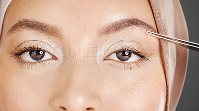 Buy stock photo Closeup portrait of traditional muslim woman using tweezers to pluck her eyebrows. Half headshot of confident arab model wearing a hijab in a studio. Cultural middle eastern grooming her facial hair