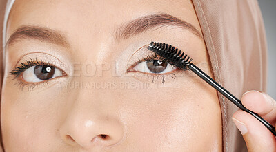Closeup portrait of a muslim woman applying mascara to her eyelashes. Headshot of a stunning arab model doing her makeup standing against a grey background. Face of a beautiful woman doing eye makeup