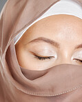 Closeup of one beautiful young muslim woman with eyes closed wearing brown headscarf posing against grey studio background. Modest female arab wearing makeup with face covered in traditional hijab