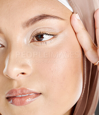 Closeup face of beautiful muslim woman wearing a hijab, posing in studio. Headshot of arab model pulling the skin by her eyes showing off her natural eyelashes and perfect smooth skin. Anti-aging