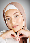 Portrait of a glowing beautiful muslim woman isolated against grey studio background. Young woman wearing a  hijab or headscarf showing her eyelash extensions and jewellery. Touching flawless skin