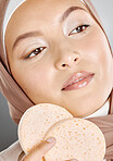 Beautiful muslim woman holding and using a pumice stone on her face against a grey studio background. Young woman wearing an hijab and doing her skincare routine. Taking care of healthy skin

