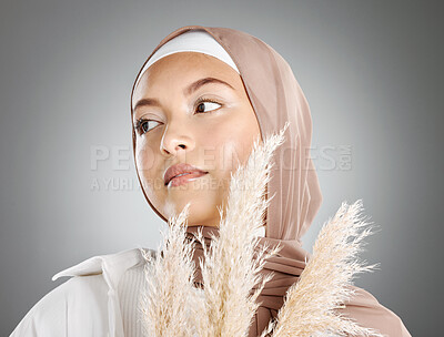 Buy stock photo One beautiful young muslim woman wearing brown headscarf holding a pampas wheat plant isolated against grey studio background. Modest female arab wearing makeup with face covered in traditional hijab
