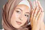 Studio portrait of beautiful muslim woman isolated against a grey background. Young woman wearing a hijab or headscarf showing traditional arab modesty holding her hands together and looking at camera