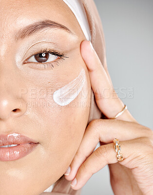 Buy stock photo Portrait of a young Muslim woman wearing a hijab or headscarf applying a cream moisturizer on her flawless skin while showing her eyelash extensions while. Applying cosmetics to maintain healthy skin
