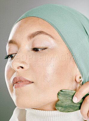 Buy stock photo Woman using a facial stone on her face. Beauty model doing  her morning skin care routine with a jade stone. Young female using a gua sha product for healthy skin.