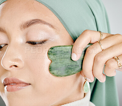 Closeup of beautiful muslim woman wearing a hijab, using a jade gua sha on face. Zoomed headshot of confident arab model sculpting face. Middle eastern woman with routine skincare and lymph drainage
