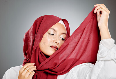 Buy stock photo A classy muslim woman wearing a red hijab or headscarf isolated against grey background with copyspace. Confident  female wrapping her head in a traditional scarf while getting dressed in a studio