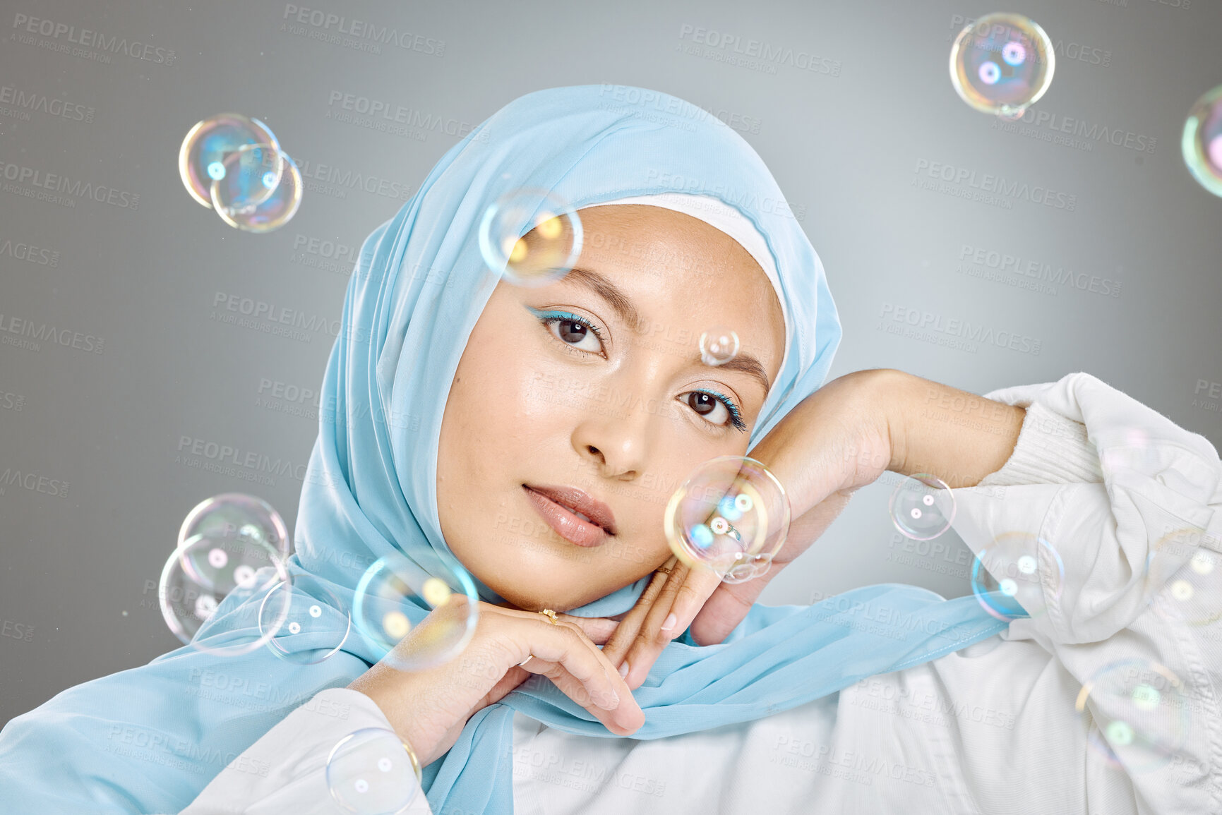Buy stock photo Portrait of a beautiful muslim woman wearing blue hijab headscarf against grey background. Arab female in a happy daydream and fantasy surrounded by the pure delight and innocence of playful bubbles
