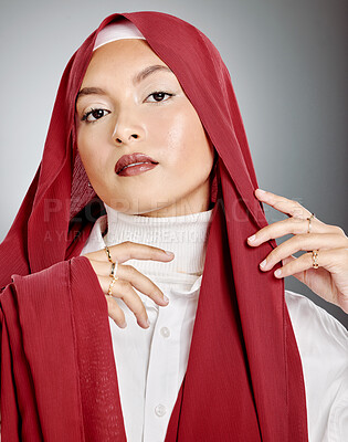 Buy stock photo Portrait of a woman wearing a red hijab against grey studio background and copyspace. Young muslim lady wearing a headscarf, posing and showing radiant skin, makeup,  eyelash extensions and jewellery
