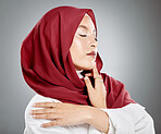 Beautiful muslim woman posing in a studio wearing a hijab. Headshot of a stunning confident arab model standing against a grey background. Fashionable woman wearing a headscarf