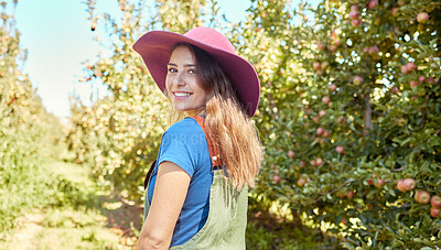 Portrait of a beautiful female farm worker standing on a fruit farm during harvest season. Young happy farmer between fruit trees on a sunny day in summer. Agricultural industry growing fresh produce