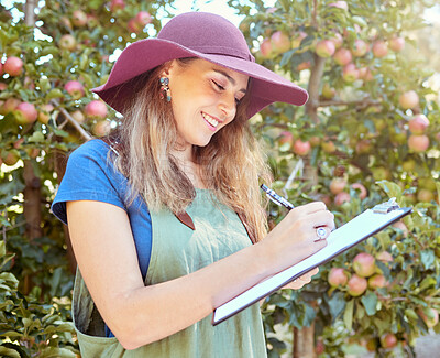 Buy stock photo Happy woman writing notes on clipboard while working on sustainable apple orchard farm on sunny day. Cheerful farmer reading checklist while planning task for harvest season of fresh organic fruit