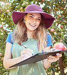 Portrait of female farm worker writing and making notes on a fruit farm during harvest season. Young smiling farmer between apple trees on a sunny day. The agricultural industry growing fresh produce