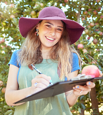 Portrait of female farm worker writing and making notes on a fruit farm during harvest season. Young smiling farmer between apple trees on a sunny day. The agricultural industry growing fresh produce