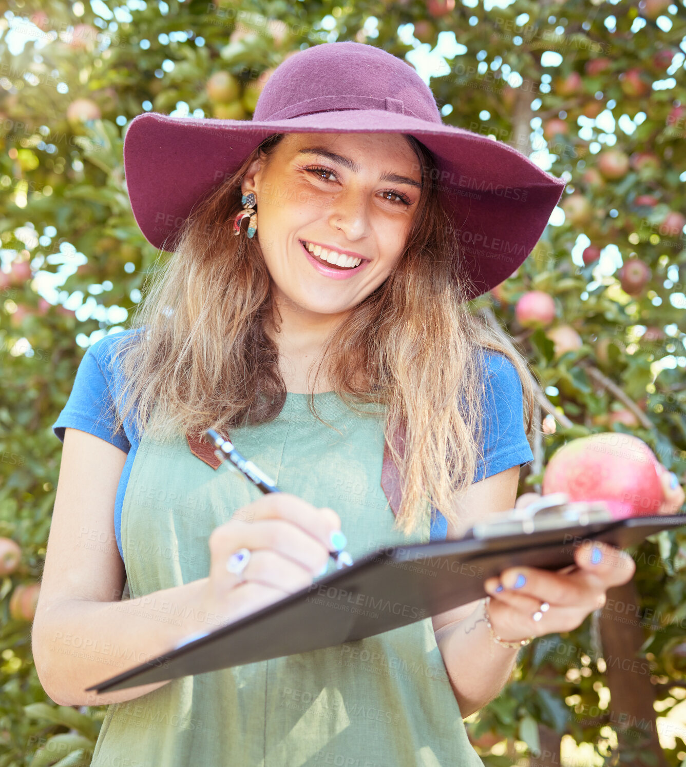 Buy stock photo Portrait of female farm worker holding an apple while writing and making notes on a orchard farm during harvest season. Agronomist doing inspection and record keeping on the quality of produce