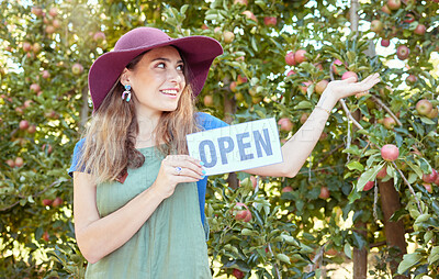 One happy woman holding open sign to advertise apple picking season on sustainable orchard farm outside on a sunny day. Cheerful farmer pointing to trees for harvesting juicy nutritious organic fruit
