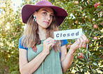 Portrait of one woman holding closed sign to advertise the end of apple picking season on orchard farm. Farmer closing agriculture business due to bankruptcy, recession, pandemic and failed economy 