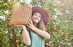 One happy woman from below holding basket of freshly picked apples from tree on sustainable orchard farm outside on sunny day. Cheerful farmer harvesting juicy nutritious organic fruit in season 