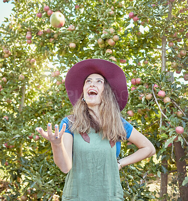 Buy stock photo Beautiful young female farmer throwing an apple on a farm during harvest season. Happy woman picking fruit in an organic and sustainable orchard. Fresh produce growing in a field for agriculture