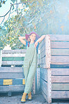 Portrait of a female farmer standing near crates on a fruit farm during harvest season. Full body low angle view of a farm worker in an orchard next to wooden crates and apple trees on a sunny day