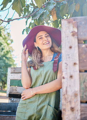 Buy stock photo Portrait of a woman in a straw hat standing under a tree next to a rustic wooden crate. One young happy female wearing a summer hat and dungaree dress in a garden on a sunny day picking apples