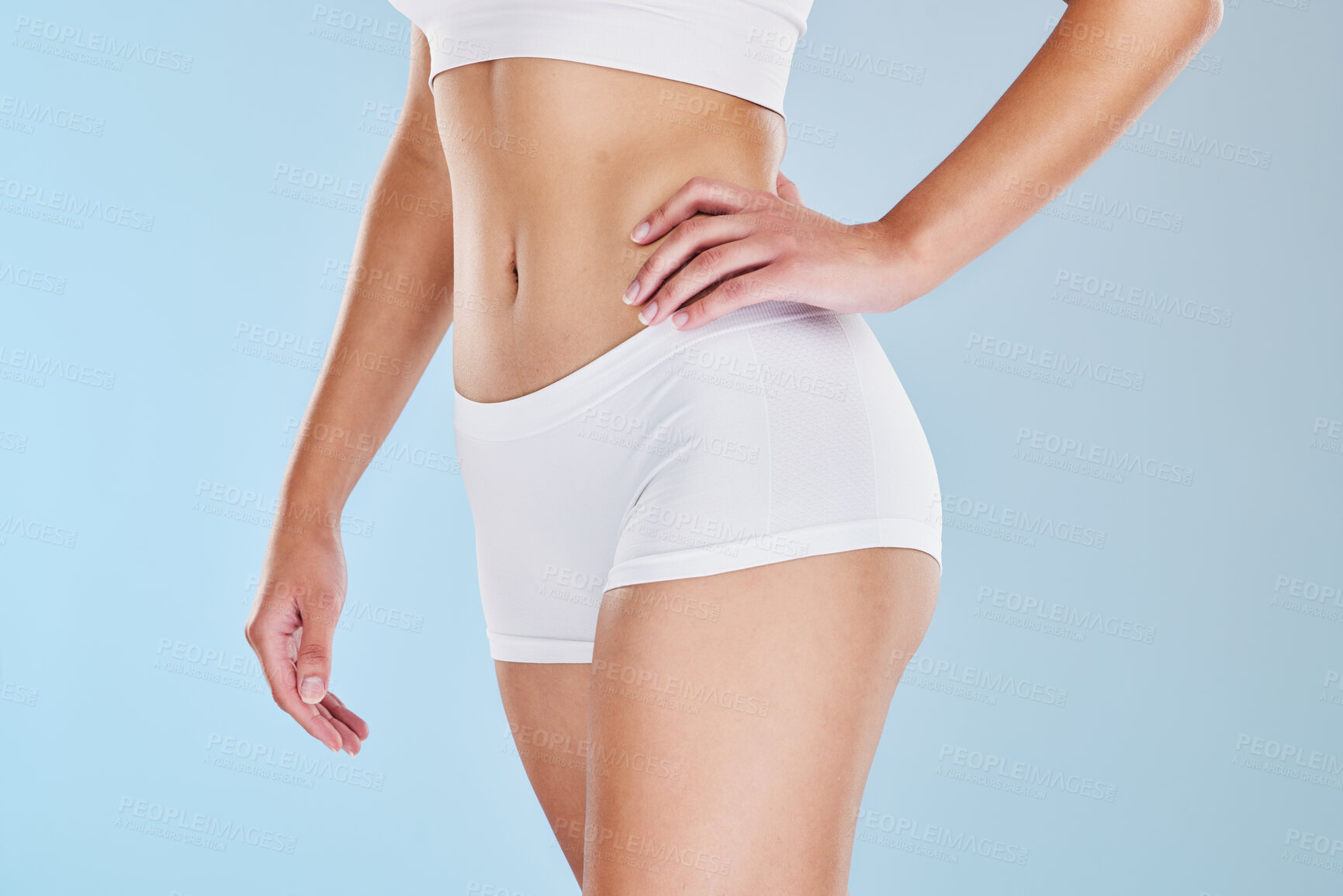 Buy stock photo Closeup of fit woman showing her stomach and body in underwear or sportswear, isolated against blue studio background with copyspace. Toned, sporty model standing alone. Slim physique and flat tummy