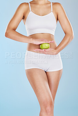 Buy stock photo Healthy toned woman dieting and holding an apple while posing in underwear against a blue studio background. Fit, sporty model standing alone, isolated with copyspace and showing a fresh snack fruit
