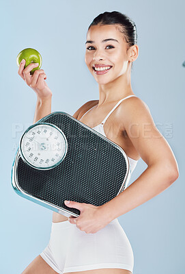 Buy stock photo Portrait of a happy young woman holding an apple and scale against blue copyspace background. Confident athletic fit female showing the benefits of a balanced diet, weight loss and healthy lifestyle
