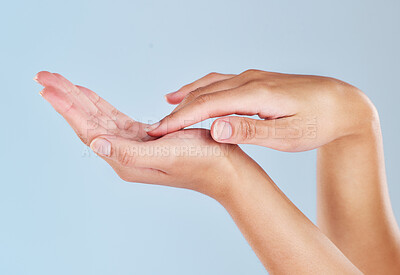 Closeup of female hands with her fingers touching her palm. Woman with soft, flawless skin applying moisturizing cream or lotion to her hand isolated on a blue background