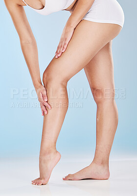 Buy stock photo Woman stroking her shaved and smooth legs isolated on a blue studio background. Slim female touching her skin after hair removal, waxing or depilation treatment. Showing her beautiful long legs 