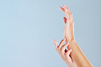 Closeup of unknown woman hands with soft skin showing manicured hands while isolated against blue studio background. Two feminine hands raised and reaching for a beauty treatment